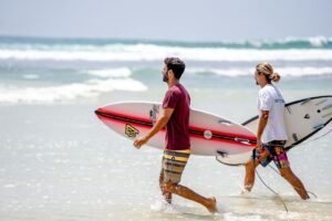 Two surfers carrying boards on a sunny day at Dambulla Beach, Sri Lanka.